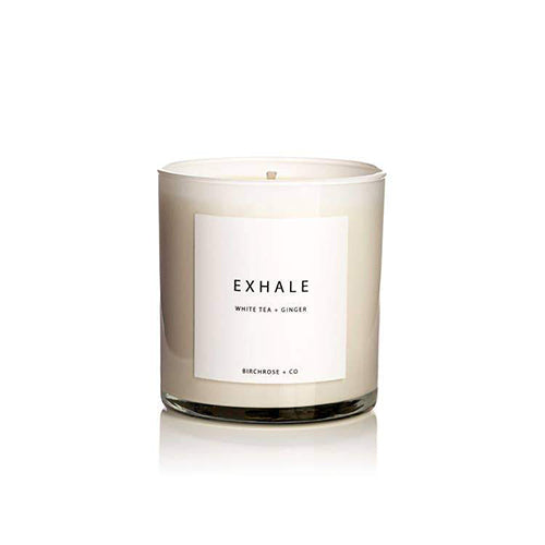 A candle in a glass container with the label "exhale, white tea and ginger". 