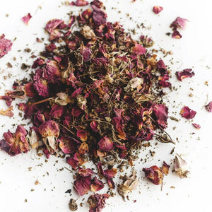 A pile of loose tea sits on a flat surface.  The tea has rose petals and a variety of dried herbs. 