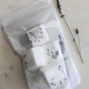 A package of 5 shower steamers in a clear bag next to a sprig of lavender.