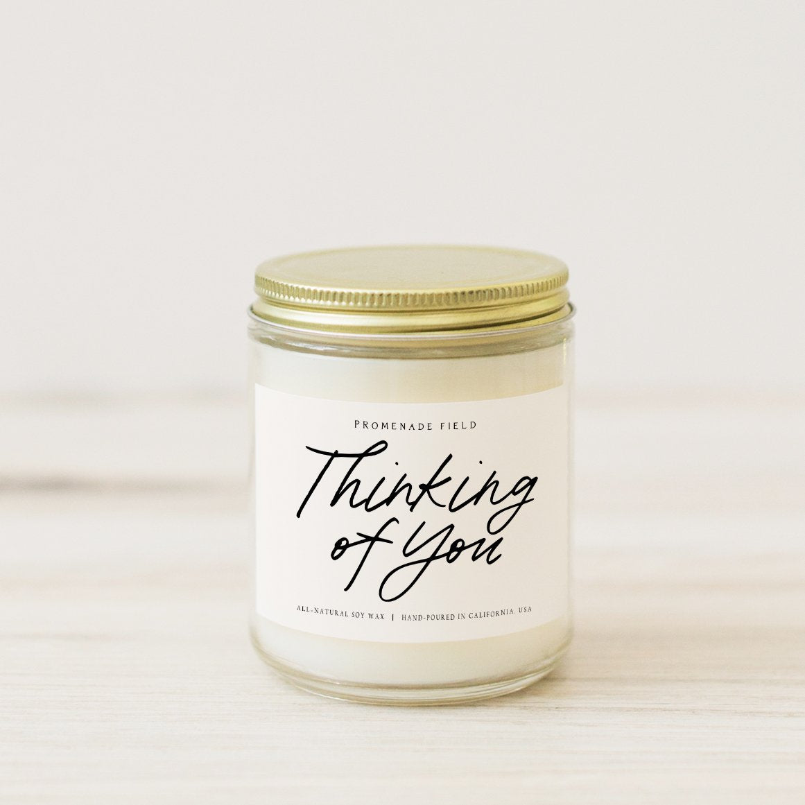 A beautiful and simple candle in a glass jar with a gold lid. Label reads "Thinking of You".