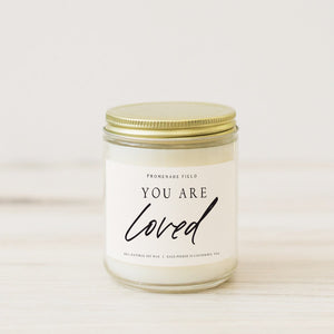 A beautiful and simple candle in a glass jar with a gold lid.  Label reads "You Are Loved".