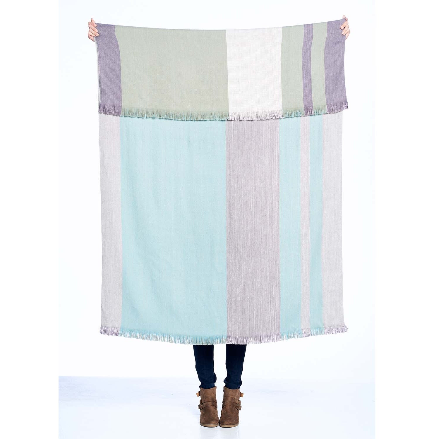 A person who cannot be seen holds up a large throw with a folded over top.  The photo is showing that the throw has colored block pattern on each side in pastel pinks, blues, and purples. 