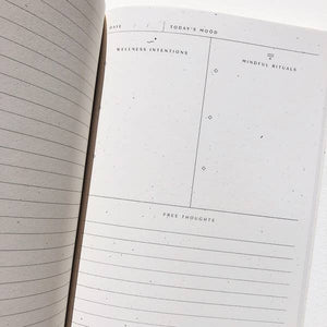 An interior photo of the Wellness Ritual Journal.  The left side reads "Wellness Intentions" and left side reads Mindful Rituals.  The bottom of the page has blank lines and a header reading "Free Thoughts". 